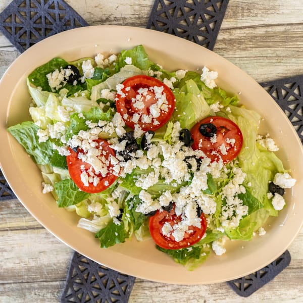 A fresh salad with lettuce, sliced tomatoes, black olives, and crumbled feta cheese in a beige bowl.