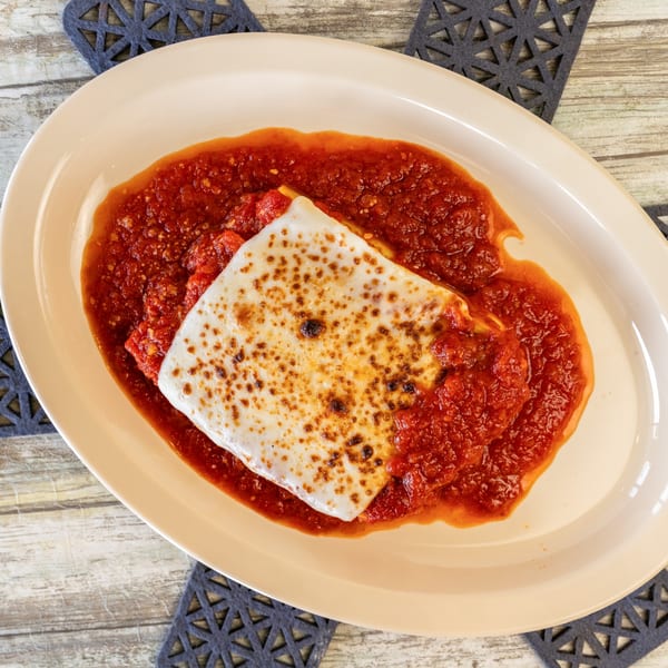 Baked lasagna with melted cheese and rich red sauce on an oval plate.