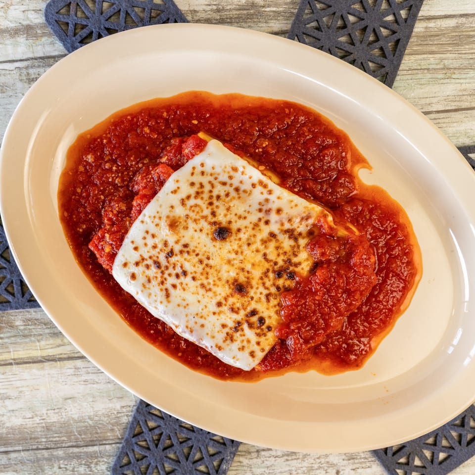 Baked lasagna with melted cheese and rich red sauce on an oval plate.