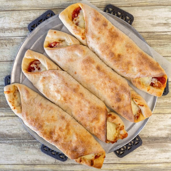 Five Romano's Pizza calzones with melted cheese and pepperoni on a metal tray.