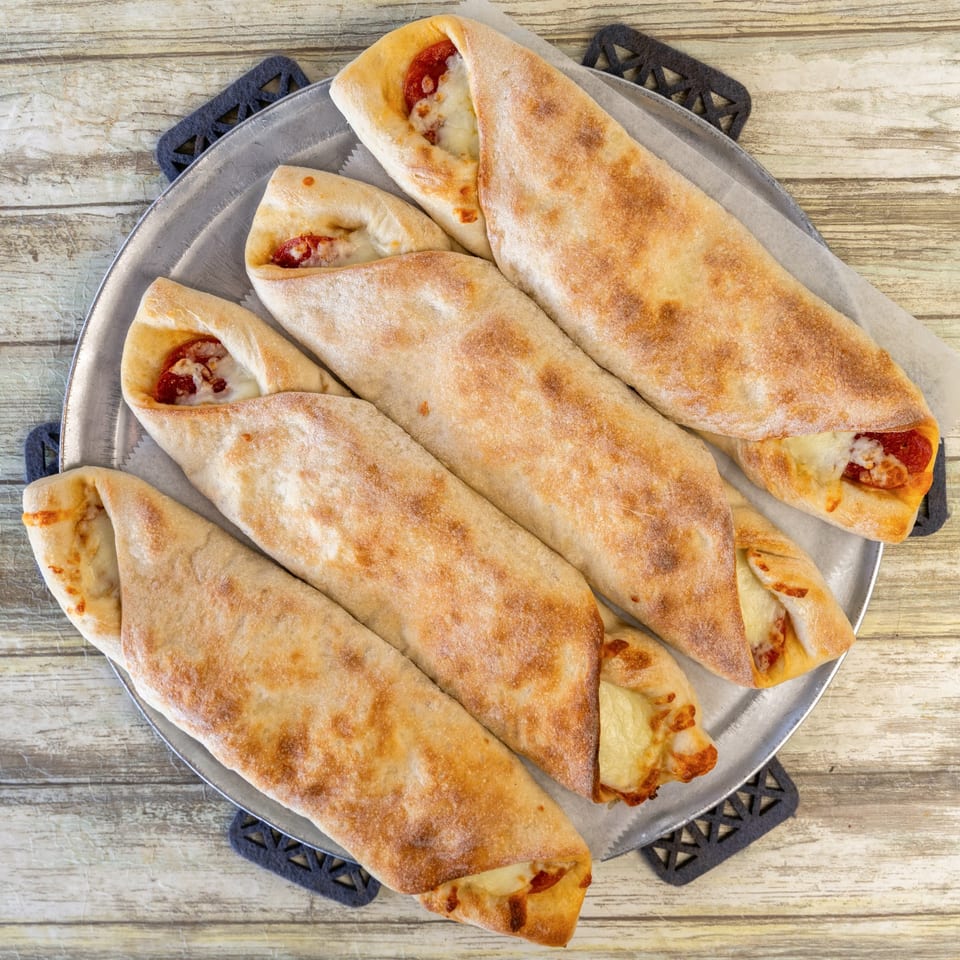 Five Romano's Pizza calzones with melted cheese and pepperoni on a metal tray.