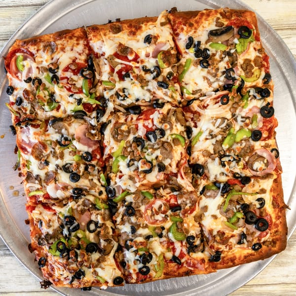 A square Romano's Pizza with pepperoni, sausage, olives, green peppers, and onions on a metal tray.