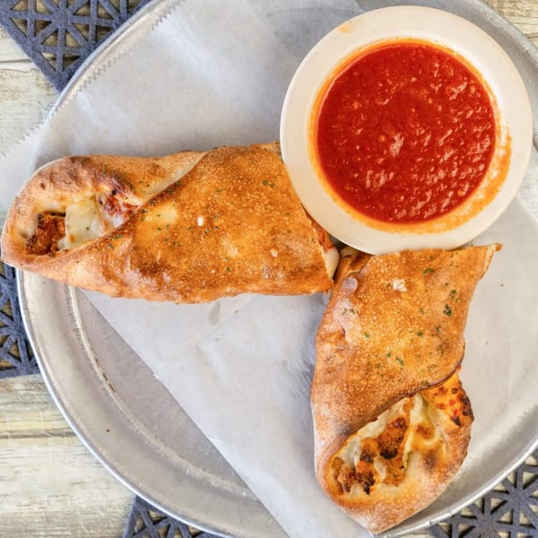 Two golden-brown Romano's Pizza calzones with melted cheese and a side of red marinara sauce.