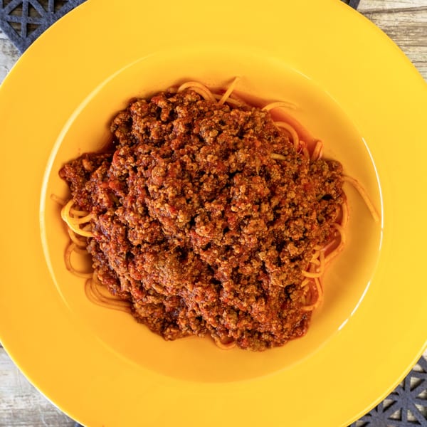 Spaghetti Bolognese with rich meat sauce in a bright yellow bowl, from Romano's Pizza.
