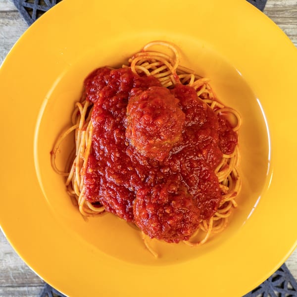 Spaghetti and meatballs with red sauce in a bright yellow bowl on a wooden table.