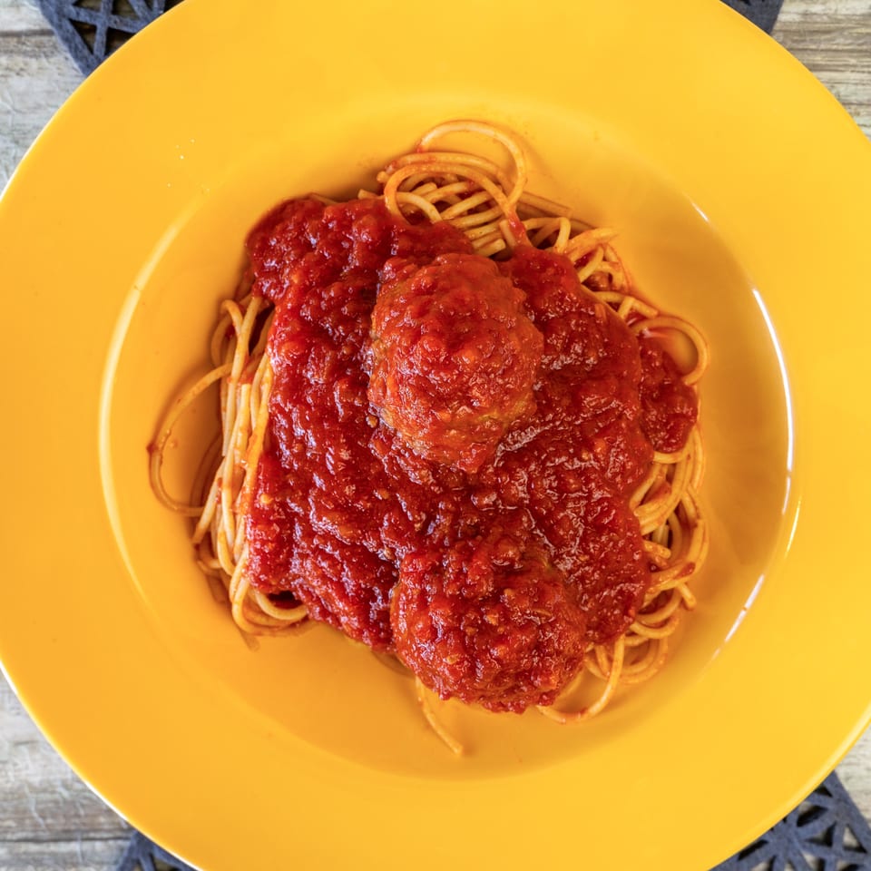 Spaghetti and meatballs with red sauce in a bright yellow bowl on a wooden table.